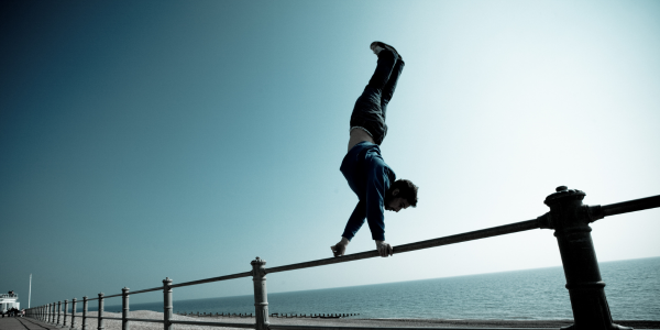 man handstand walking on a bar by the ocean