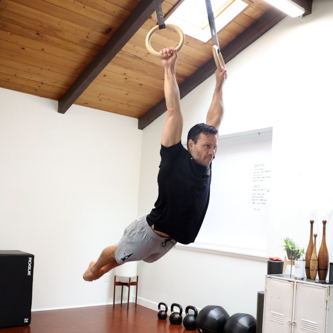 Image of a man performing a kipping ring muscle-up to promote the kipping ring muscle up program in the Power Monkey Training app. 