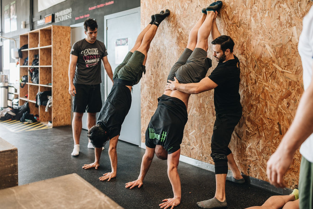 Photo of Dave Durante spotting an athlete performing a handstand against a wall at a Power Monkey Fitness Course. 